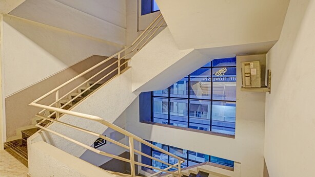 A modern hotel interior with a staircase, a sign indicating the 3rd floor, and a view of the hotel exterior through large windows. - Itsy Hotels Flowers Park (Nashik)