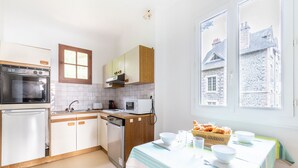 A modern kitchen with a built-in oven, microwave, and dishwasher. There is a dining table set with a box of gourmet bread and bowls. - Breathtaking view of the sea for 7 people in Pléneuf (Pléneuf-Val-André)