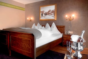 Een net opgemaakt bed met witte lakens, een houten hoofdbord en een nachtkastje met een fles en glaasjes.