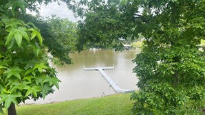 A tranquil lake with a dock, surrounded by lush green trees and a grassy area.