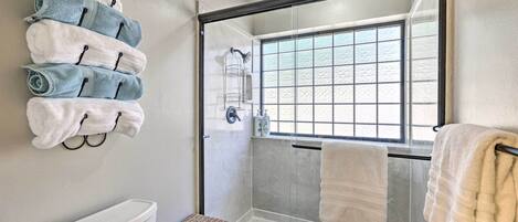 A bathroom with a glass-enclosed shower, a toilet, and a towel rack with multiple towels.