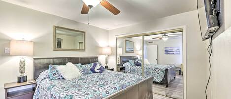 A bedroom with a large bed, a ceiling fan, a mirror, and a TV mounted on the wall.