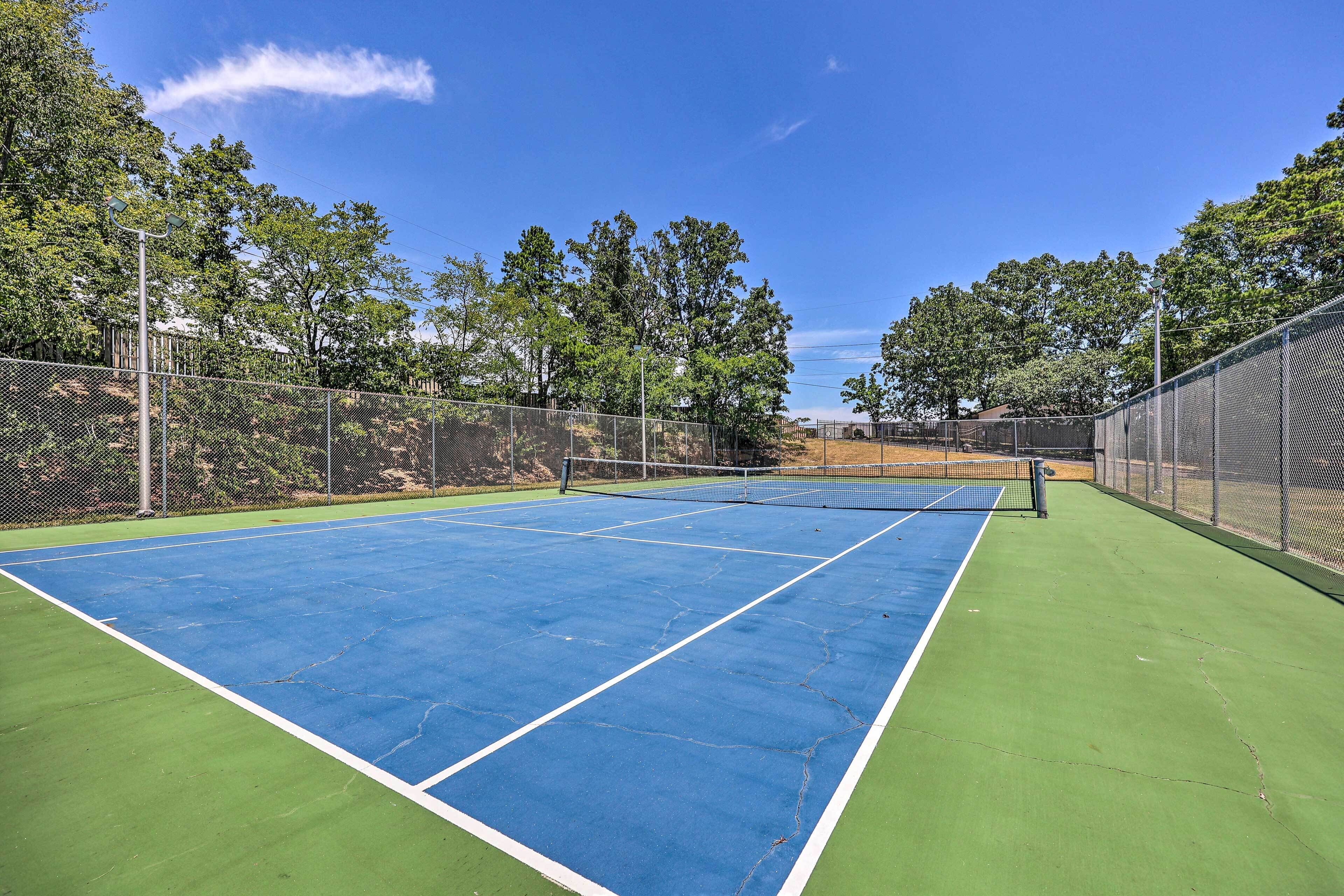 A tennis court with a net, surrounded by a fence and trees.