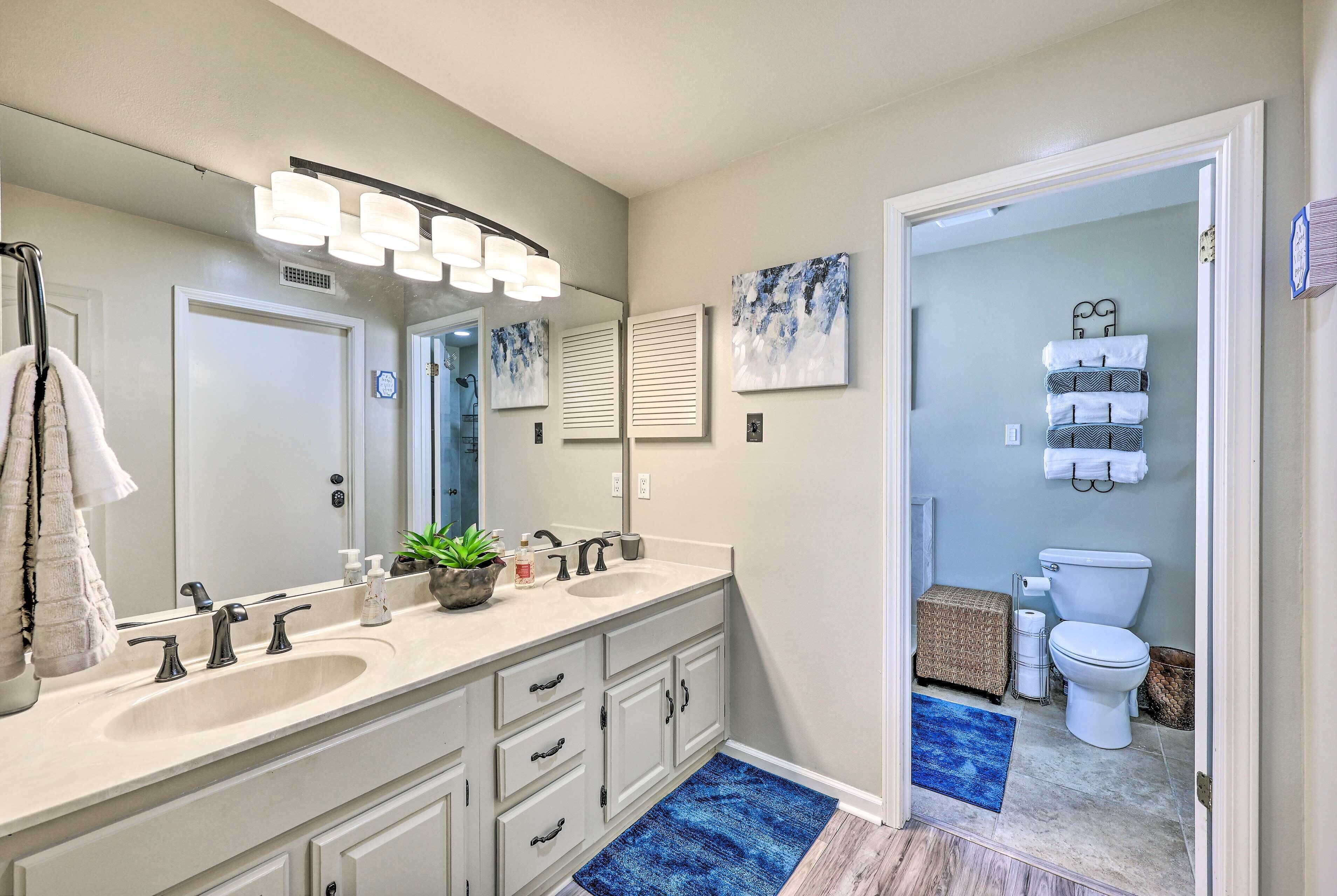 A modern bathroom with a double sink vanity, a large mirror, and a toilet visible through an open door.