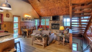 A rustic cabin interior with a dining area, sofa, fireplace, and a staircase.