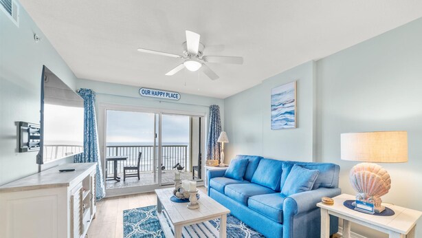 A room with a blue sofa, a white coffee table, a lamp, and a view of the ocean through a sliding door.