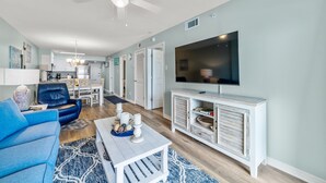 A modern living room with a blue sofa, a coffee table with decorative items, a white TV stand, and a ceiling fan.
