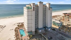 A multi-story hotel with a pool, located near a beach with a clear view of the ocean.