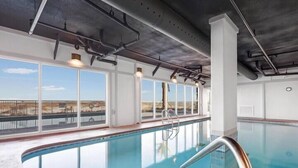 An indoor swimming pool with clear glass walls, a metal ladder, and a view of the outdoors.