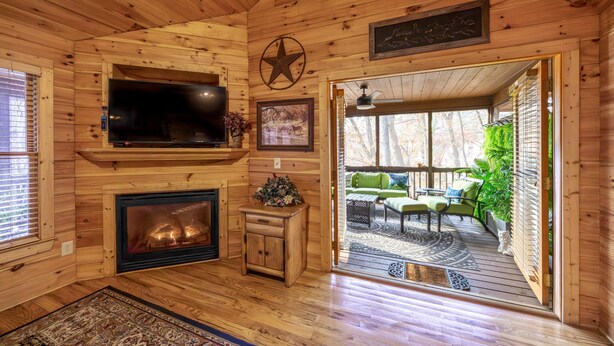 A cozy cabin interior with a fireplace, television, and a view of the outdoor deck.