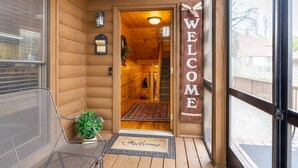 A wooden cabin entrance with a 'WELCOME' sign, a small rug, and a metal chair outside.