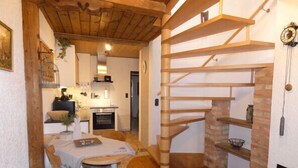 Een rustiek interieur met een houten eettafel, stoelen, een open haard en een spiltrap.