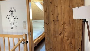 Een houten interieur met een bed, een plant en een deur naar een andere kamer.