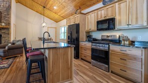 A modern kitchen with wooden cabinets, a central island, stainless steel appliances, and a stone fireplace.