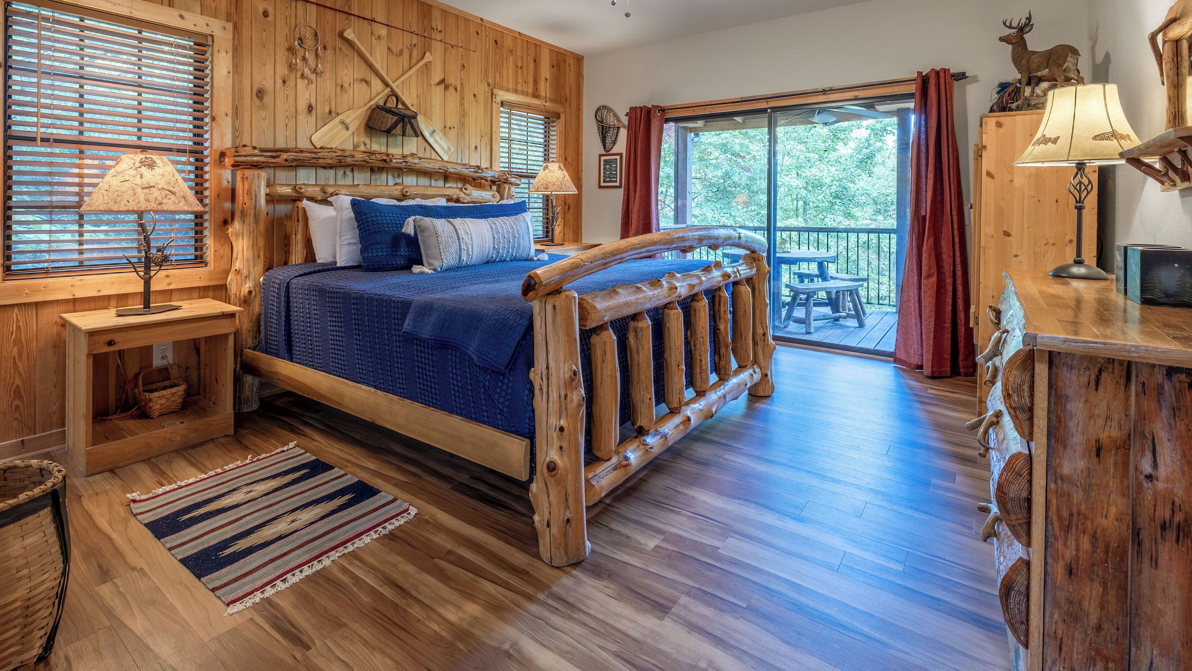 Un dormitorio rústico de madera con una cama grande, cabecera de madera y vistas al exterior a través de una puerta corrediza de vidrio.