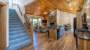 A spacious kitchen with a stone fireplace, wooden ceiling, and a large island.
