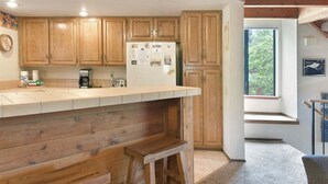 A kitchen with wooden cabinets, a white refrigerator, and a wooden bar counter. - Snowflower 53: Spacious, Partial Mountain Views (Mammoth Lakes)