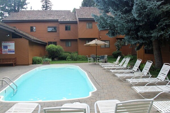A swimming pool with lounge chairs and a patio area, surrounded by a brick walkway and wooden buildings. - Snowflower 53: Spacious, Partial Mountain Views (Mammoth Lakes)
