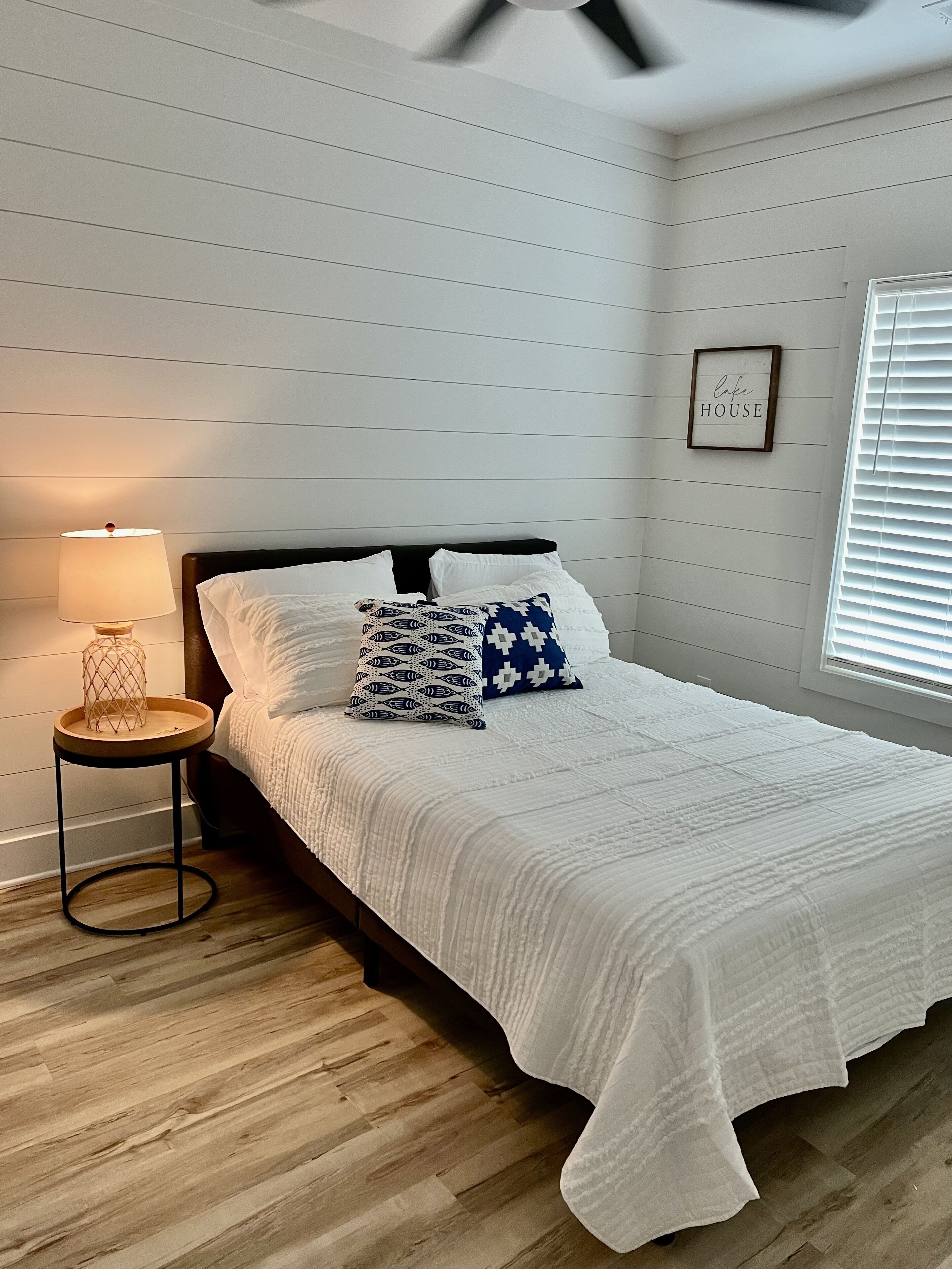 A neatly arranged bedroom with a bed, a bedside lamp, and a framed sign on the wall.