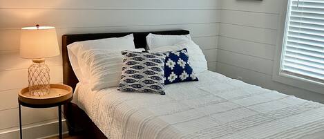 A neatly arranged bedroom with a bed, a bedside lamp, and a framed sign on the wall.