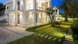 A modern two-story house with a balcony, a well-lit driveway, and a landscaped garden with a palm tree. - WLofts 12 by Klodge - cozy design holiday suite (Olbia)