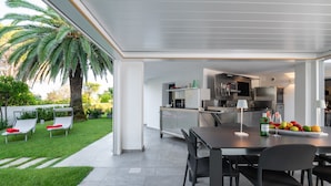 A modern kitchen with stainless steel appliances, a dining area with a table and chairs, and a patio with a palm tree and lounge chairs. - WLofts 12 by Klodge - cozy design holiday suite (Olbia)