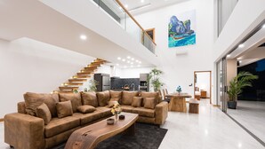 A spacious living area with a brown leather sofa, a wooden coffee table, and a dining table with chairs. A staircase with wooden steps leads to an upper level. - `Villa Majesta`Amazing View, luxury 4br Pool villa (Koh Samui)