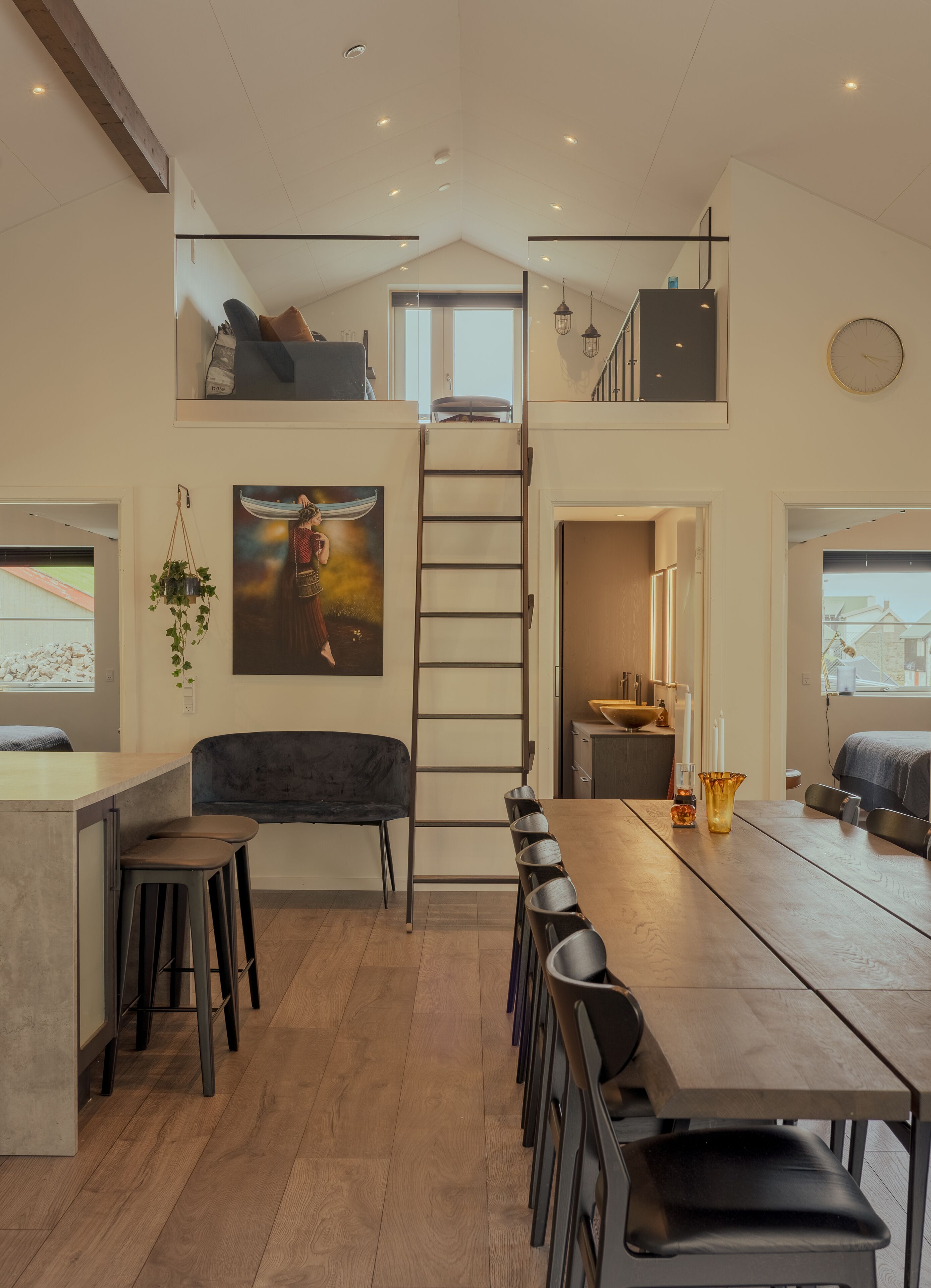 A modern loft-style kitchen with a long dining table, bar stools, and a staircase leading to an upper level.