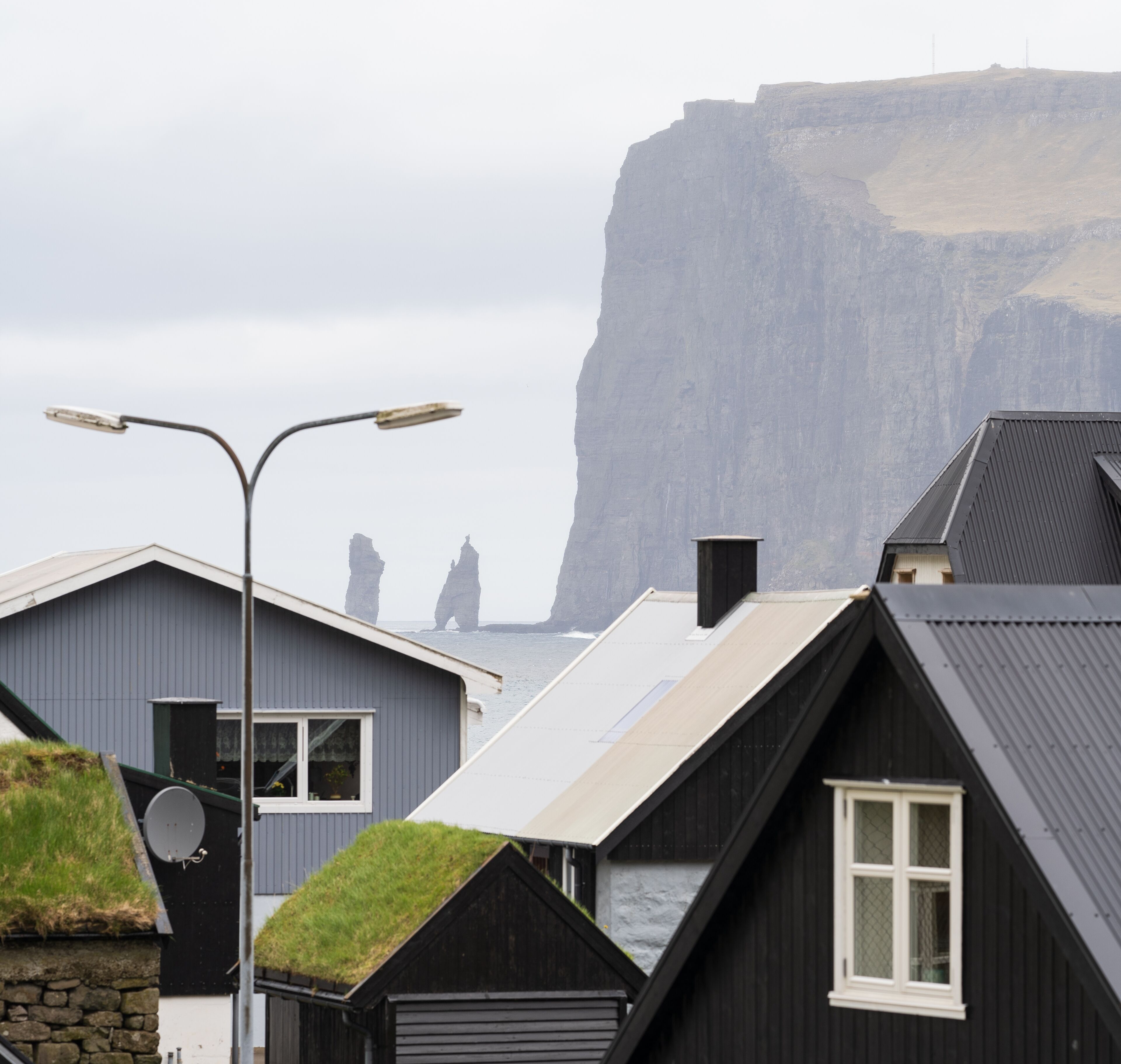 A coastal building with a steep roof, a street lamp, and a view of a cliff.