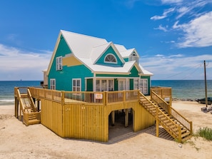 Une maison de plage dotée d’une terrasse en bois, d’un escalier et offrant une vue sur l’océan.