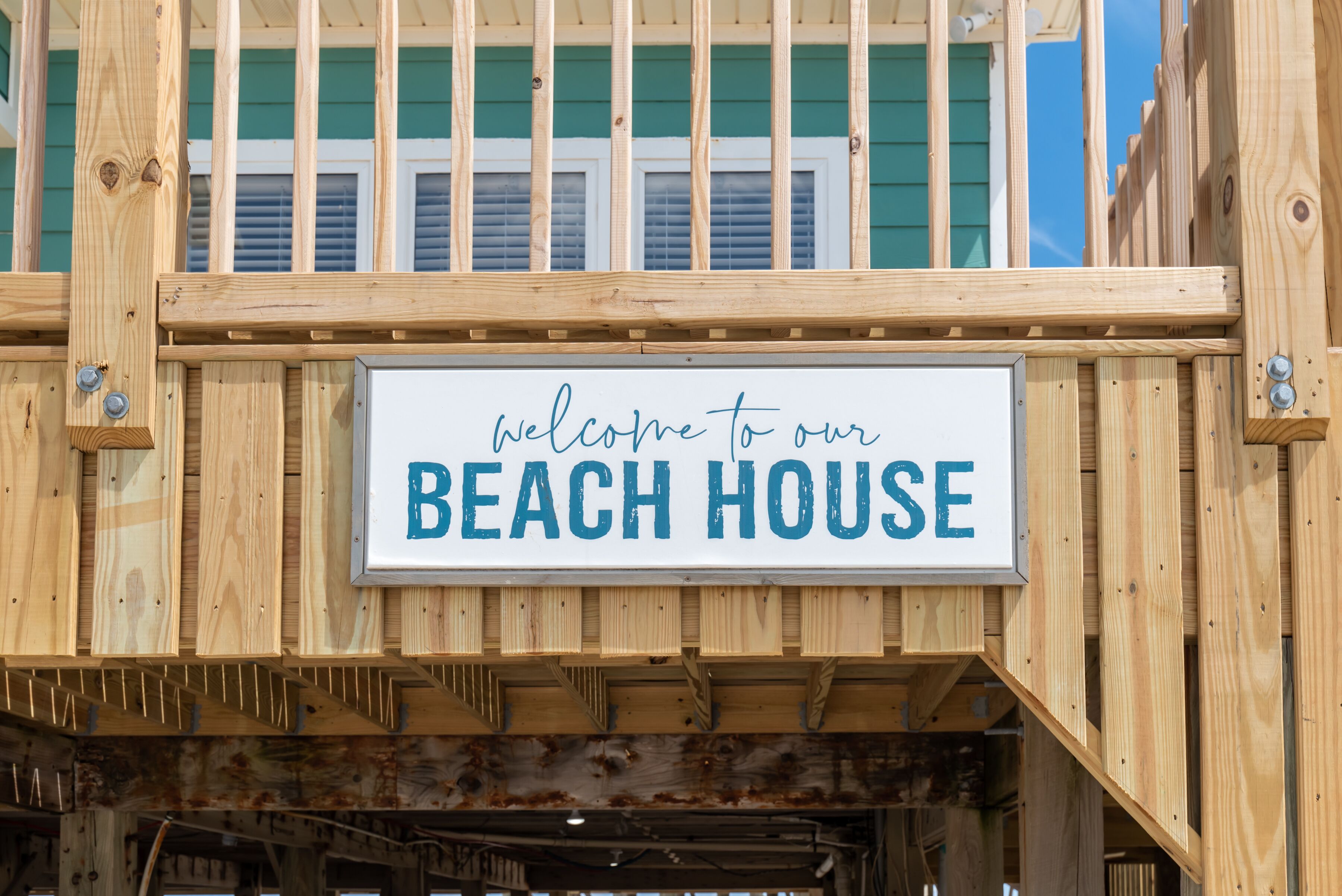 A wooden sign with "welcome to our BEACH HOUSE" written on it.