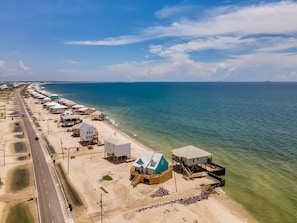 An aerial view of a coastal area with a row of beach houses, a road, and the ocean. - The Boat House - 106 Westward Ho 4 Bedroom Home by RedAwning (Dauphin Island)
