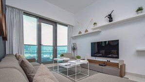 Una sala de estar moderna con un sofá grande, una mesa de centro, un televisor y un balcón con vista a la ciudad.