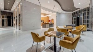 Un moderno vestíbulo de hotel con techo curvo, suelo de mármol y sillas tapizadas de color amarillo alrededor de una mesa central.