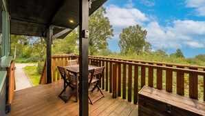 A wooden deck with a table and chairs, overlooking a grassy area with trees. - The Wood Hatch Cabin at Ancarraig Lodges, Loch Ness (Drumnadrochit)