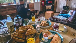 A cozy cabin-style room with a wooden interior, a fireplace, a television, and a breakfast spread on a wooden table. - The Wood Hatch Cabin at Ancarraig Lodges, Loch Ness (Drumnadrochit)