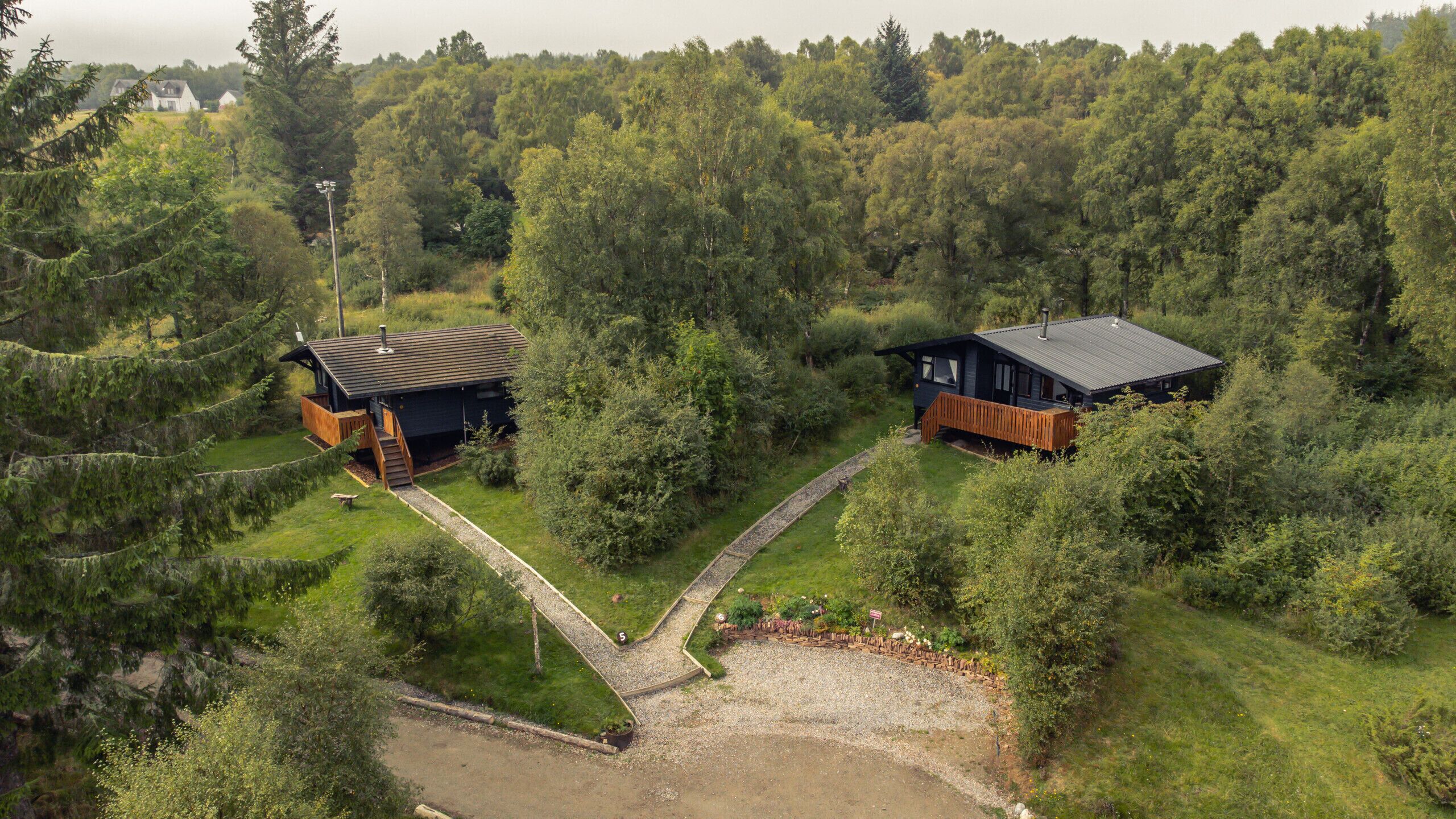 Two cabins in a forested area with a gravel path connecting them.