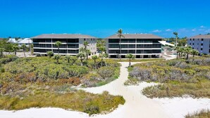 A beachfront hotel with a central pathway leading to a parking area, surrounded by dense vegetation and palm trees.