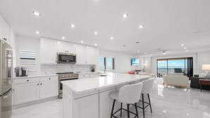 A modern kitchen with white cabinetry, a central island with bar stools, a built-in oven, and a microwave.
