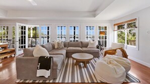A spacious living room with a sectional sofa, a round coffee table, and a large window with a view of the outdoors. - The Mill-Lauderdale Lakes Getaway |Breathtaking Views |Kayaks |15 Minutes to Skiing |Pier |Firepit (Elkhorn)