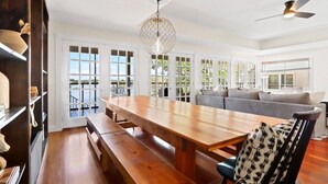 A spacious dining area with a wooden table and benches, a chandelier, and a view of the outdoors through large windows. - The Mill-Lauderdale Lakes Getaway |Breathtaking Views |Kayaks |15 Minutes to Skiing |Pier |Firepit (Elkhorn)