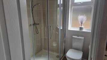 A modern bathroom with a glass-enclosed shower, a white toilet, and a window with a potted plant.