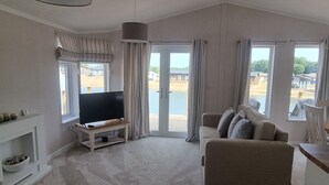 Ein geräumiges Wohnzimmer mit einem Flachbildfernseher, einem beigefarbenen Sofa und einem großen Fenster mit Blick auf Strand und Gebäude.