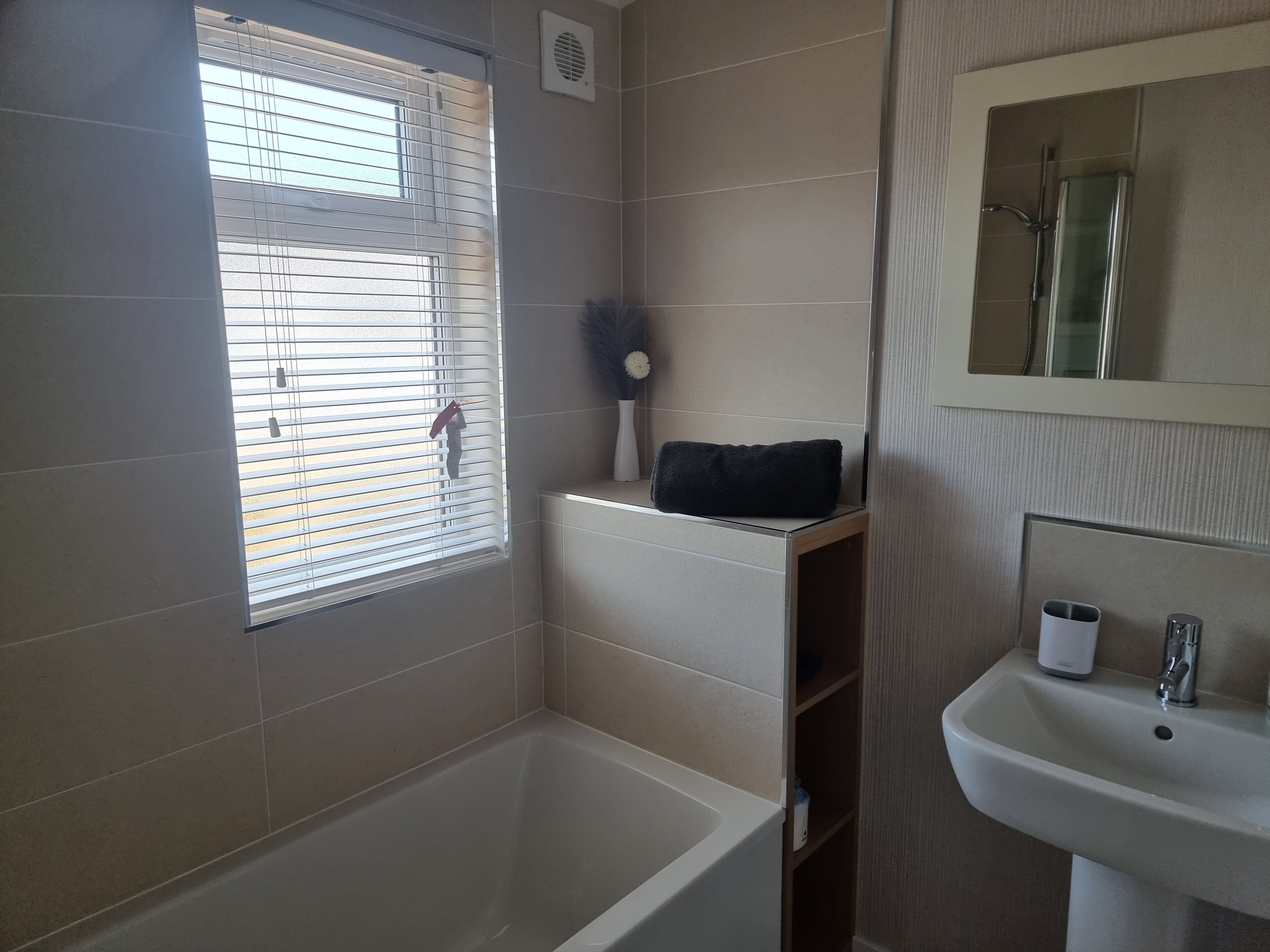 A bathroom with a bathtub, a sink, a window with blinds, and a mirror.