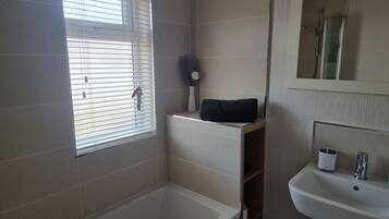 A bathroom with a bathtub, a sink, a window with blinds, and a mirror.