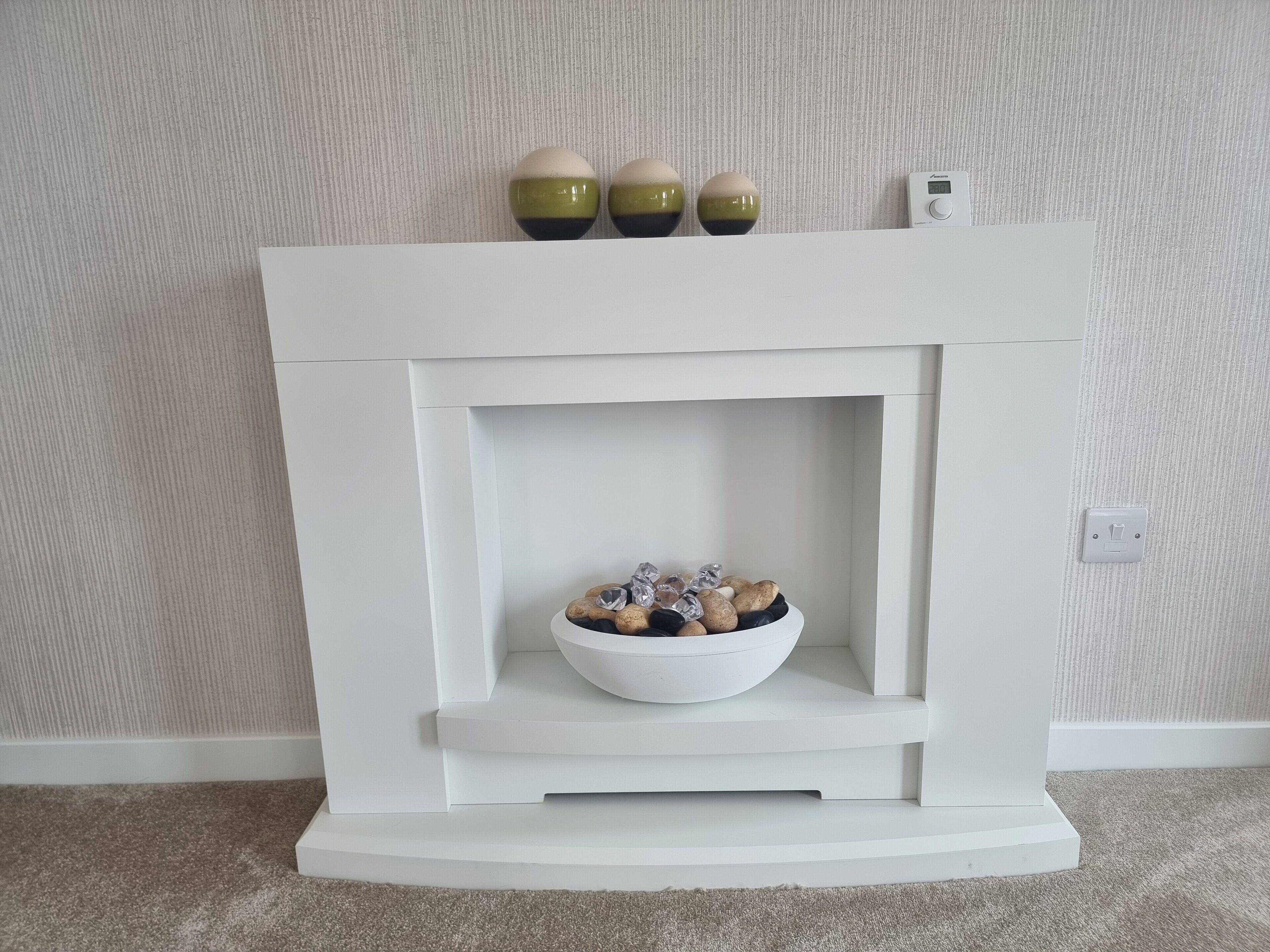 Ein weißer Kamin mit einer Schale dekorativer Steine und drei kugelförmigen Ornamenten darauf.