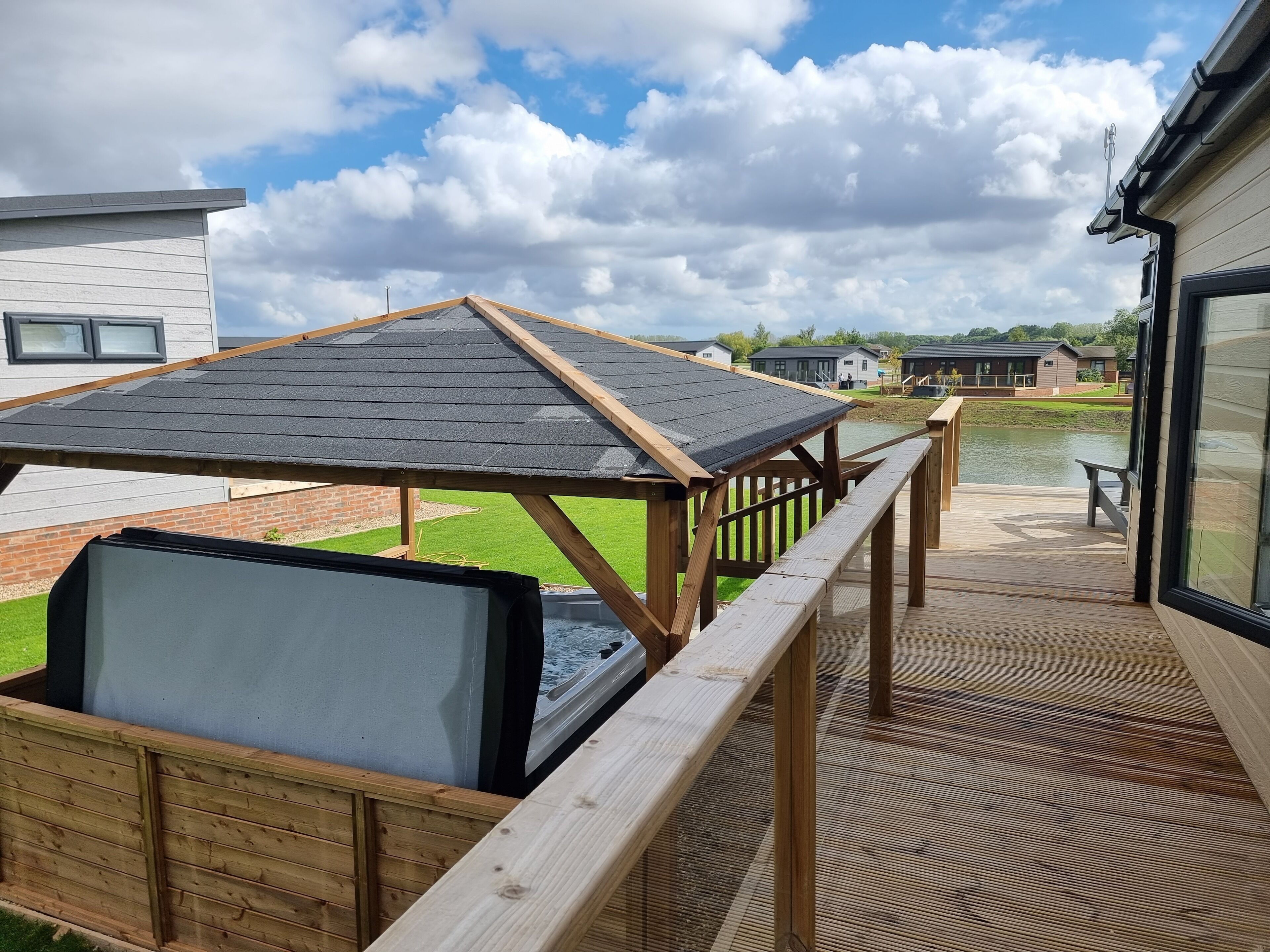 Een terras met houten hekwerk, een jacuzzi en uitzicht op een meer en huizen op de achtergrond.