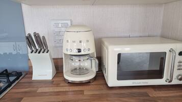 Una cocina con una cafetera blanca, un microondas blanco y un juego de cuchillos.