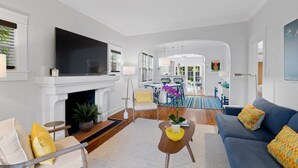 Uma sala de estar moderna com lareira, televisão e sofá. Ao fundo, há um espaço de jantar com mesa e cadeiras.