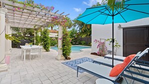 Um pátio com piscina, móveis brancos e um pergolado florido.